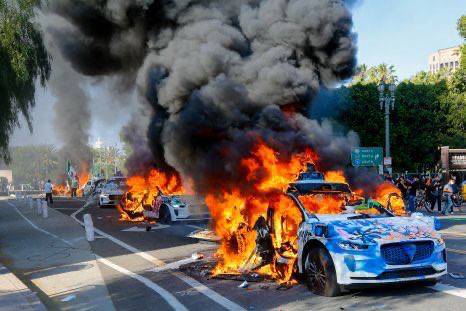 Burning Wamo delivery car during LA riots, surrounded by debris and smoke